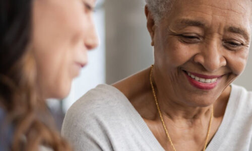 A woman and an older person smiling at each other.